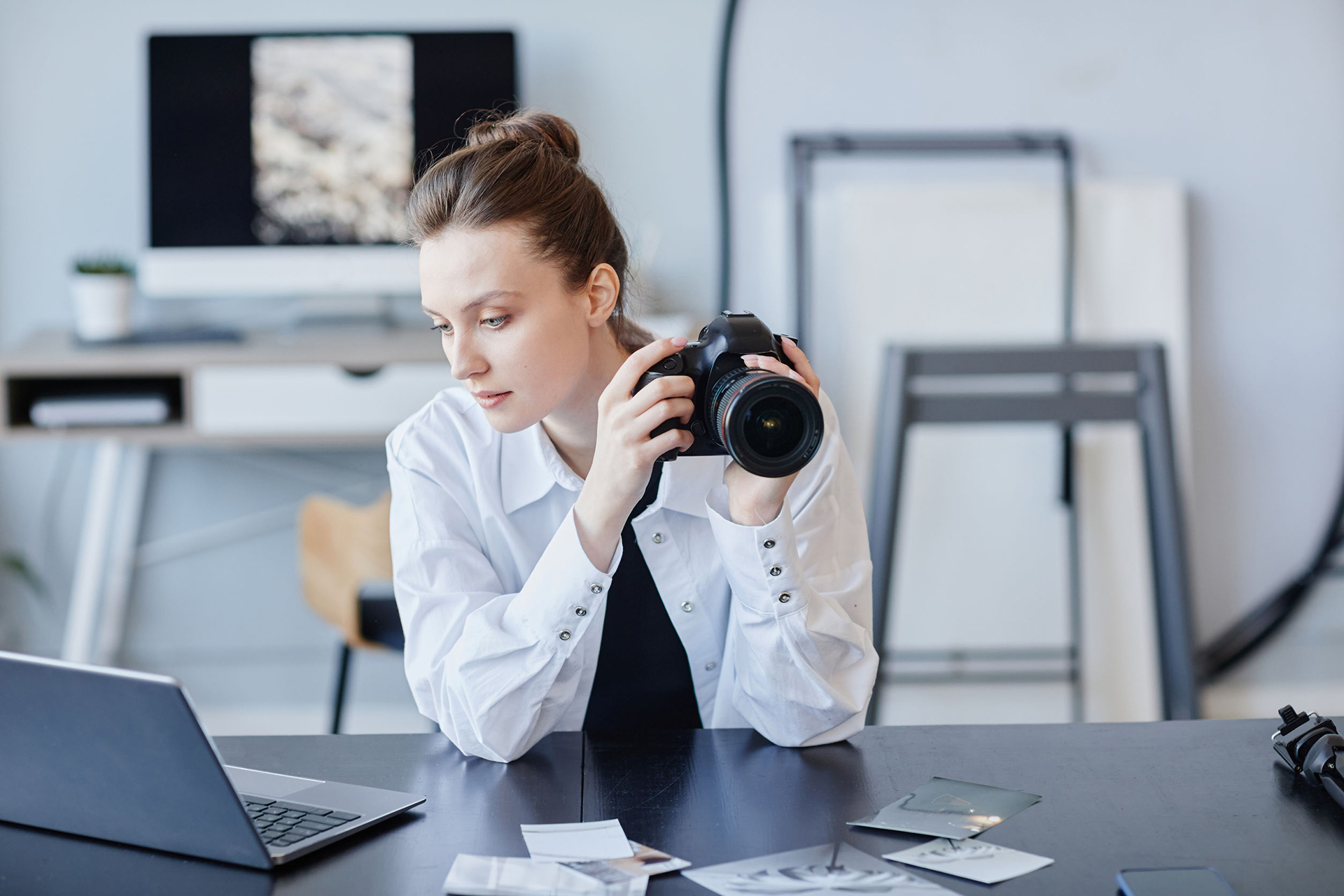 Portrait of young female photographer using laptop and photo camera in minimal studio setting, copy space